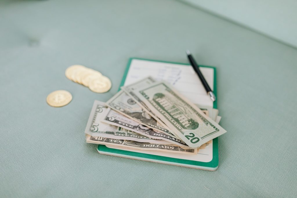 Several US dollar banknotes and coins placed on a notebook with a pen next to it.