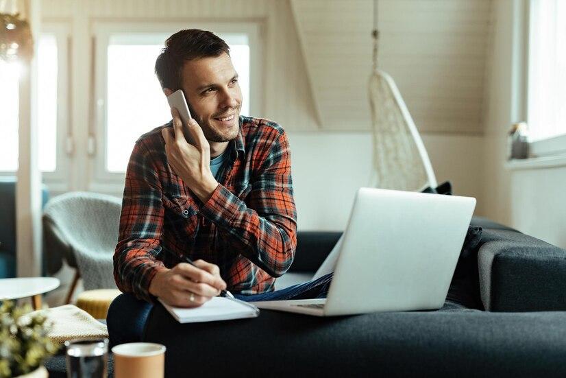 A young happy man taking notes while communicating on a cell phone.