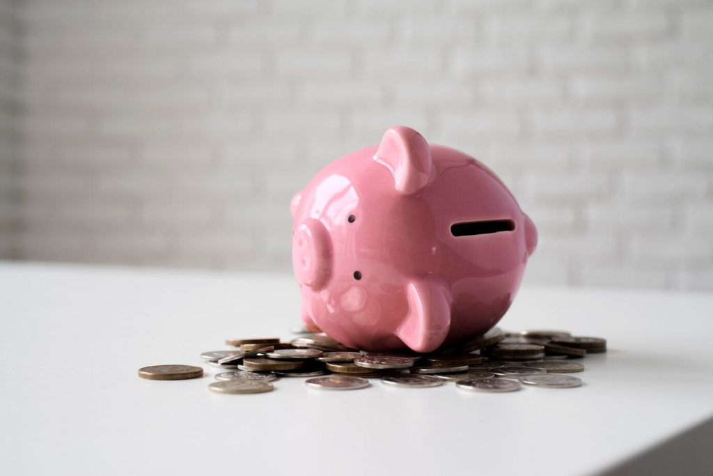 A pink piggy bank with coins around.