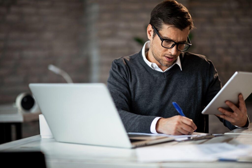 A businessman working on touchpad and writing reports on a paper in an office.